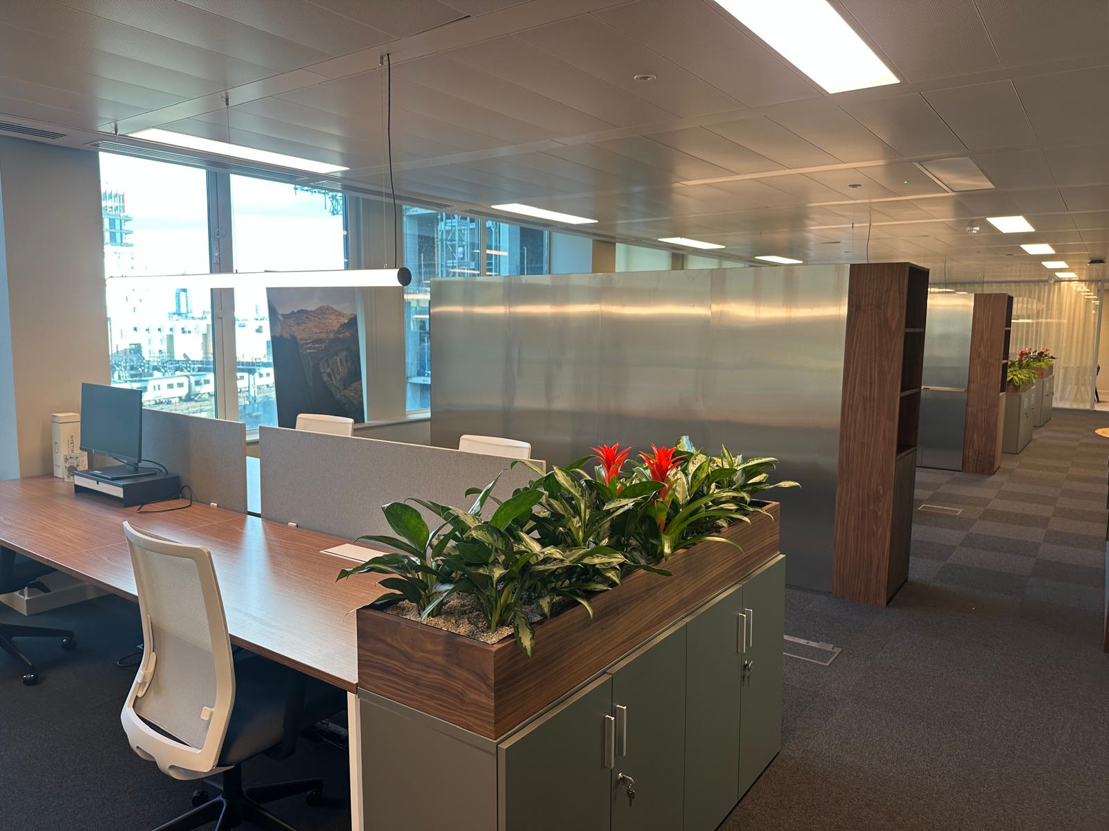 Desk banks divided by walnut planters and a brushed-steel partition